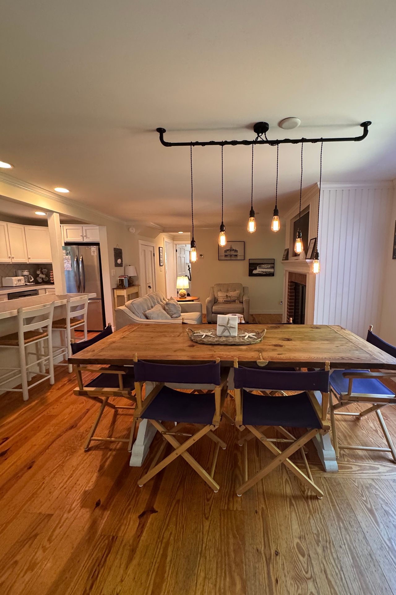 Open-plan dining and living room with a large wooden table, pendant lights, and kitchen island.