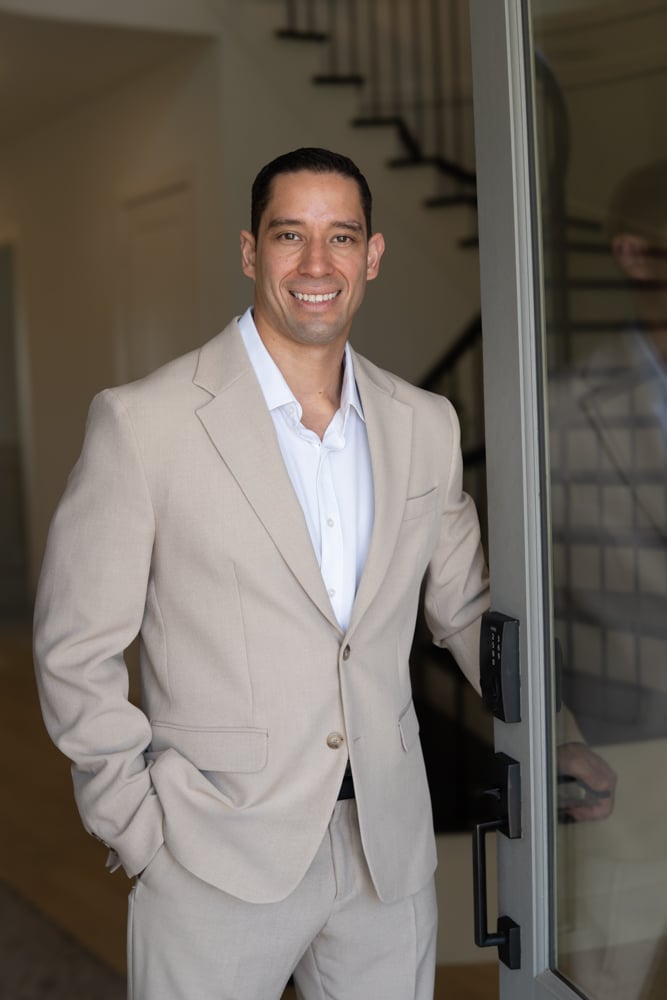 Steve Enriquez standing in a doorway in a light beige suit.