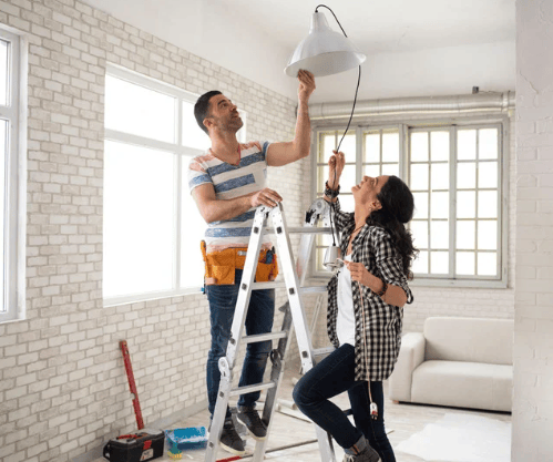 A couple adjusts a pendant light in a bright living room with white brick walls.