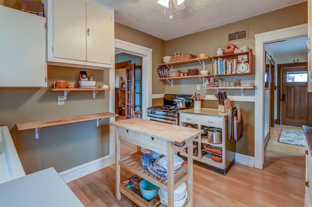 Kitchen with a central wooden worktable, open dish shelves, and a gas range.