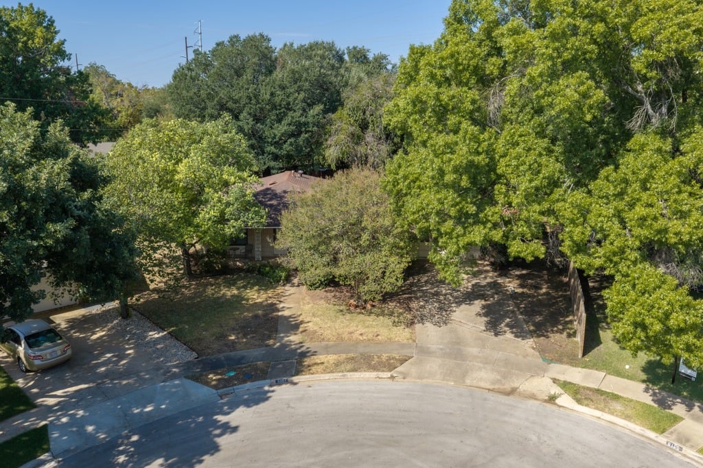 Aerial view of a tree-shaded home, driveway, and curved street.