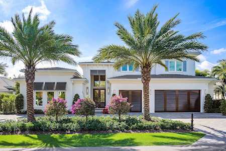 Modern white two-story home framed by palm trees, with a double garage and landscaped lawn.