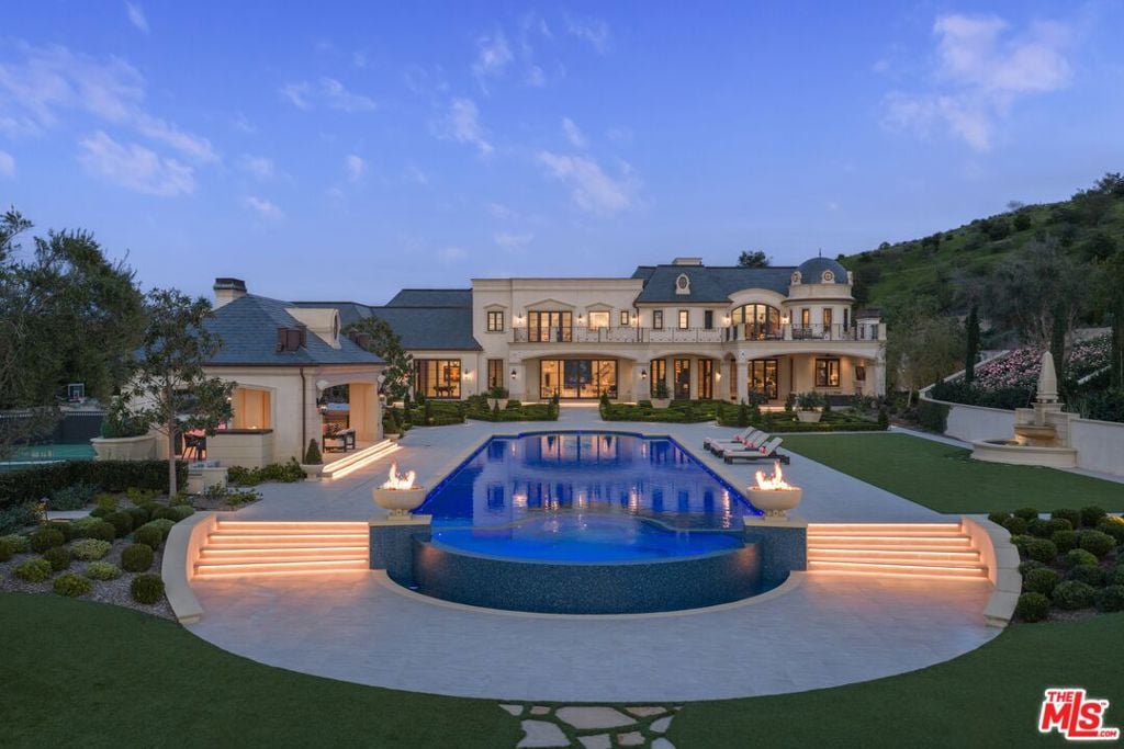 Luxury home with a blue-lit pool, curved steps, and landscaped grounds at dusk.