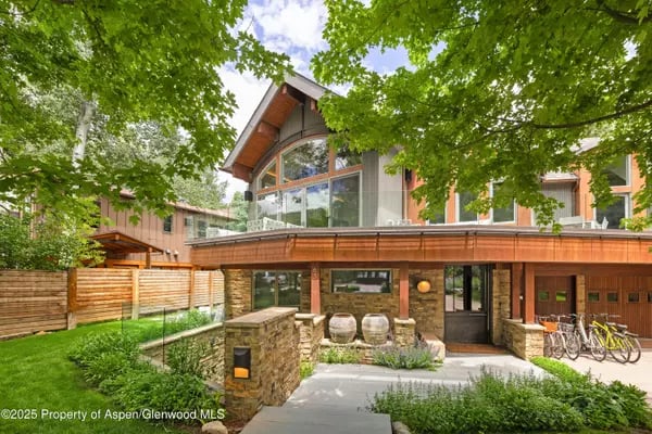 Modern home with a broad wood balcony, stone facade, and leafy trees.