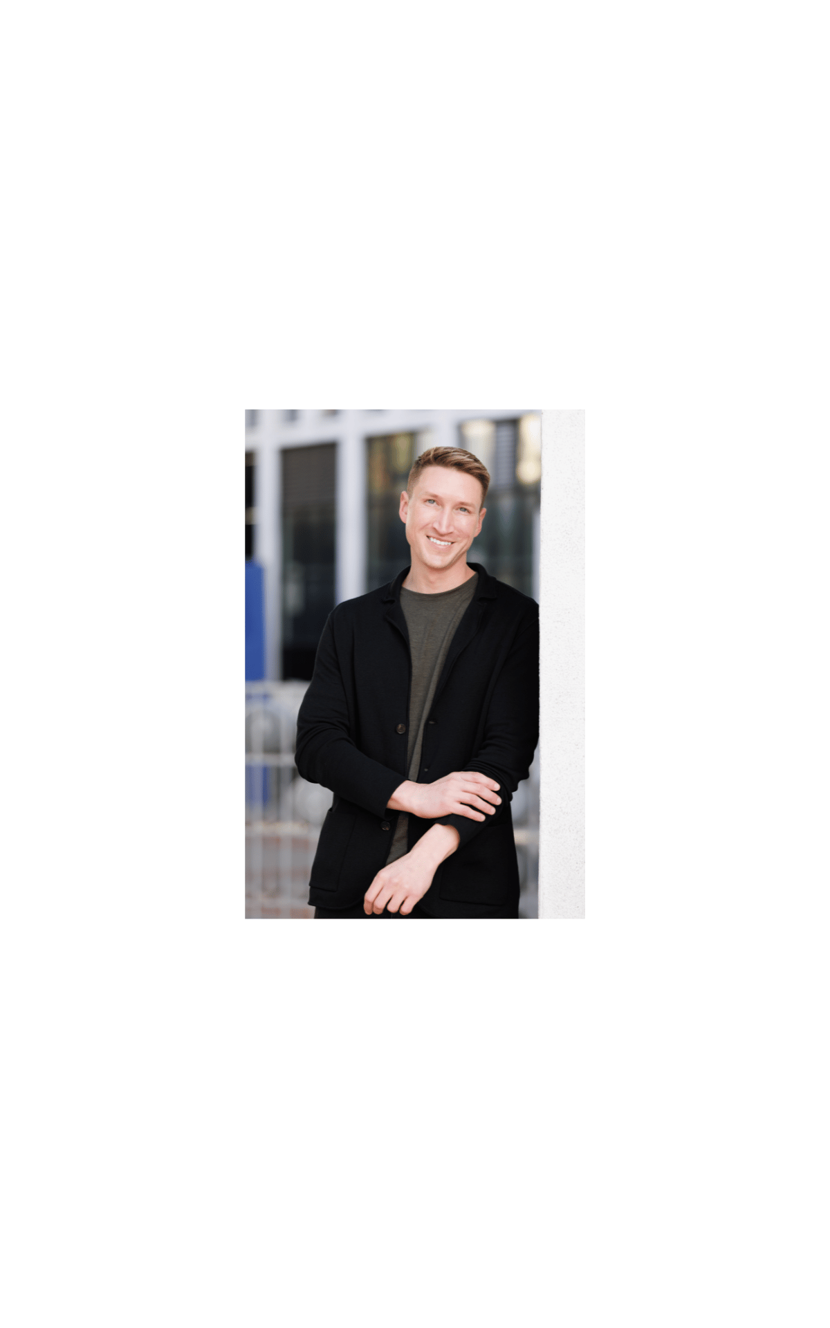 Smiling man in a black jacket leaning against a light-colored pillar