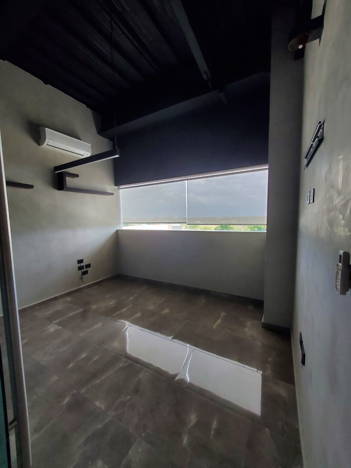Empty office with glossy tile floors, a dark exposed ceiling, and a wide shaded window.