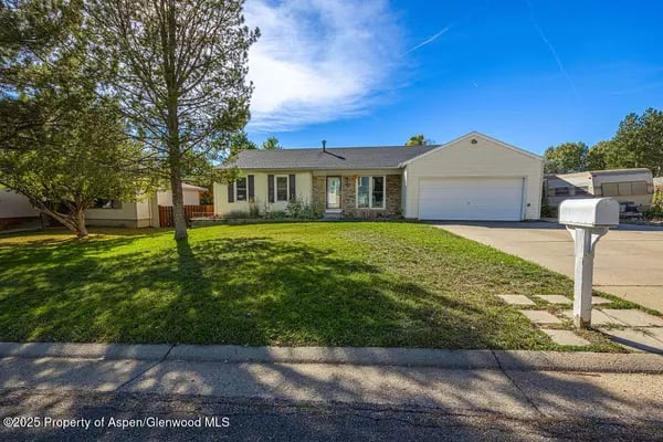 Single-story home with attached garage, broad lawn, mature trees, and a curbside mailbox.