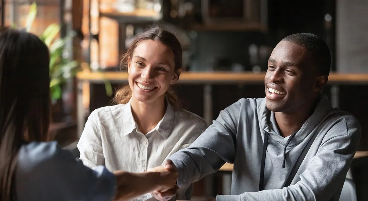 Smiling couple shake hands with a real estate agent during a meeting.
