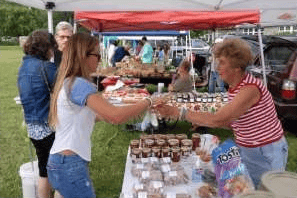 A customer and vendor exchange goods across a table at an outdoor farmers market.