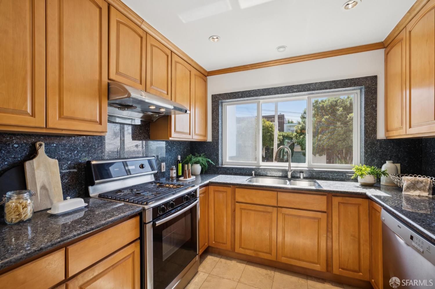 Kitchen with honey-toned wood cabinets, dark granite counters, and a wide window above the sink.