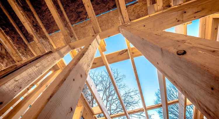 A view of an unfinished house interior, showcasing exposed beams, framing, and construction materials scattered throughout.