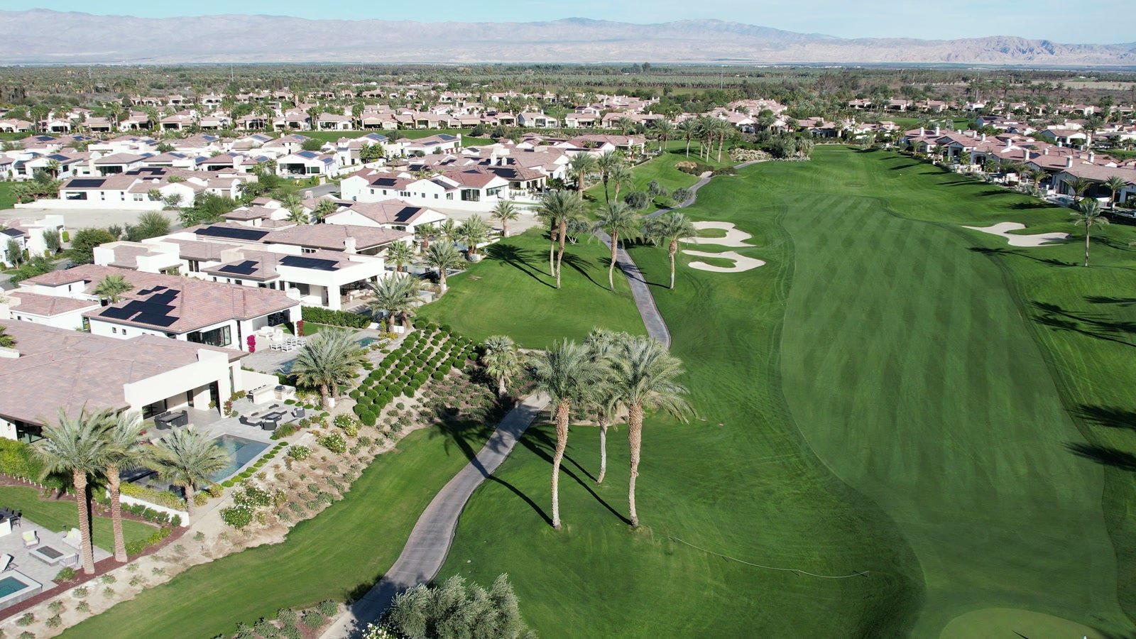 Aerial view of a South La Quinta golf community with homes, fairways, palm trees, and mountains