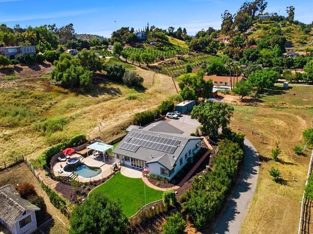 Aerial view of a rural home with rooftop solar panels and a swimming pool.