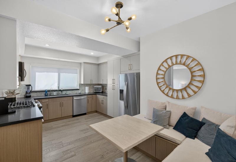 Open-plan apartment kitchen with light wood cabinetry, stainless steel appliances, and a dining table beside a cushioned bench.