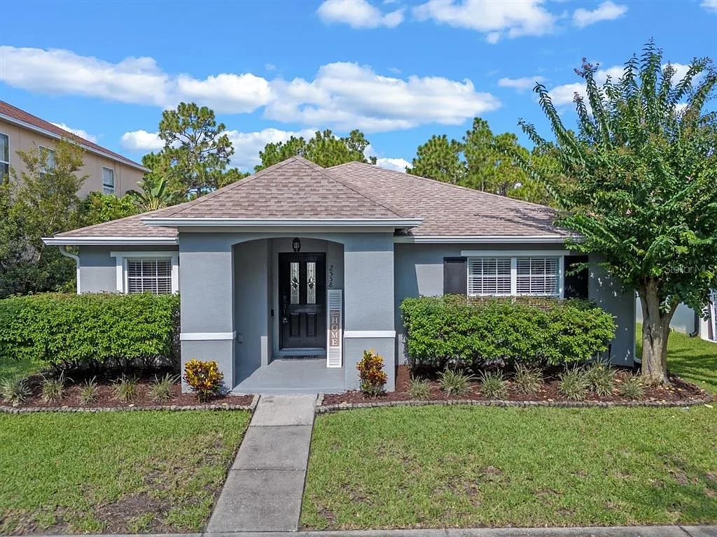 Gray single-story home with a covered entry, trimmed hedges, and a front lawn.