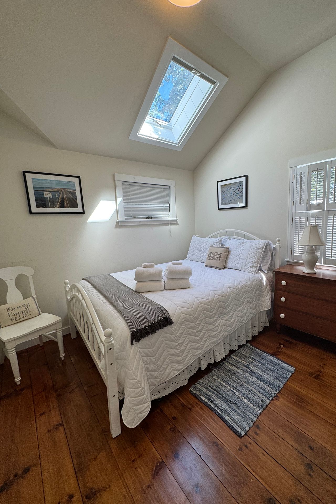 White-quilted bed beneath a skylight in a bright bedroom with dark wood floors.