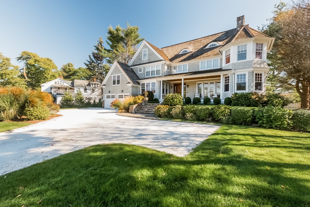 Gray shingle home with multiple gables, landscaped garden, and broad white driveway.