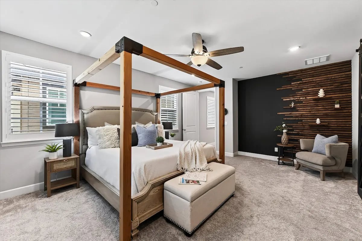 Staged bedroom with a wooden canopy bed, carpeted floor, and dark accent wall.