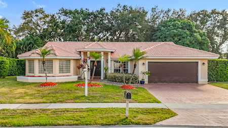 Single-story beige home with a red tile roof, two-car garage, and palm trees in the front yard.