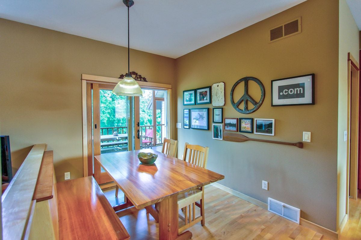 Dining room with a long wooden table, benches, framed art, and glass doors to a deck.