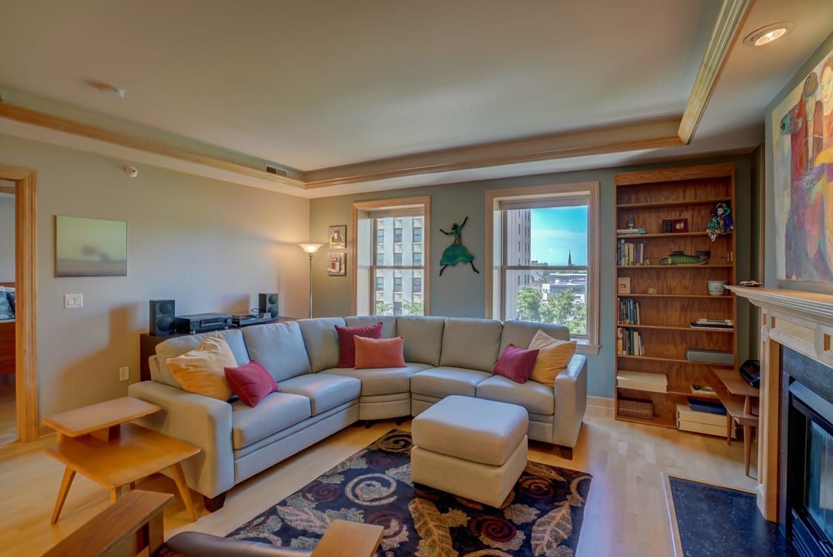 Living room with a sectional sofa, built-in bookcase, fireplace, and city views through two windows.