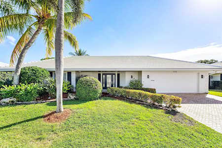 Single-story white home with a palm tree, trimmed hedges, and a paved driveway.
