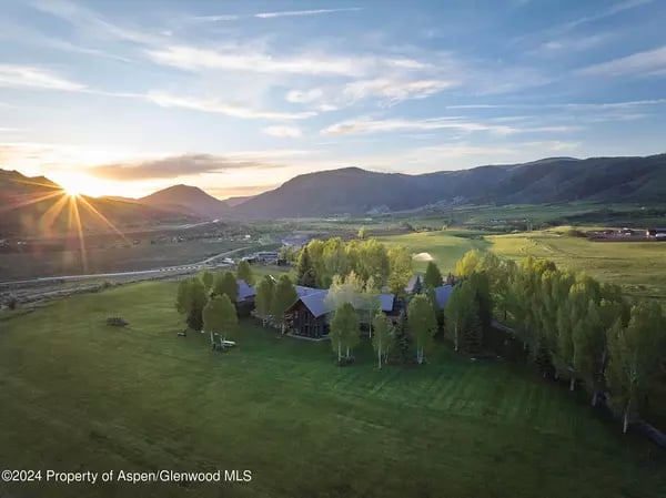 Aerial view of a tree-surrounded home in a green mountain valley at sunset.