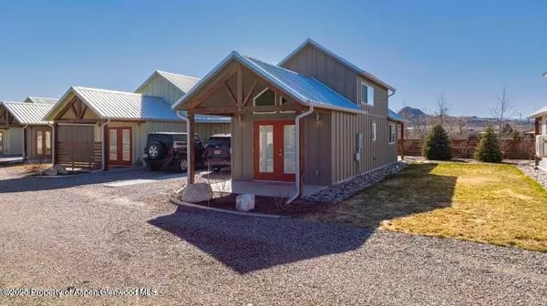 Small brown home with a red entry door, metal roof, and covered parking.