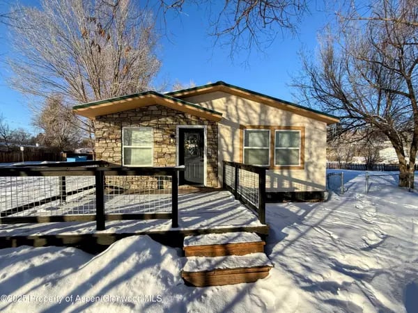 Single-story home with a stone facade and black-railed entry ramp in a snowy yard.
