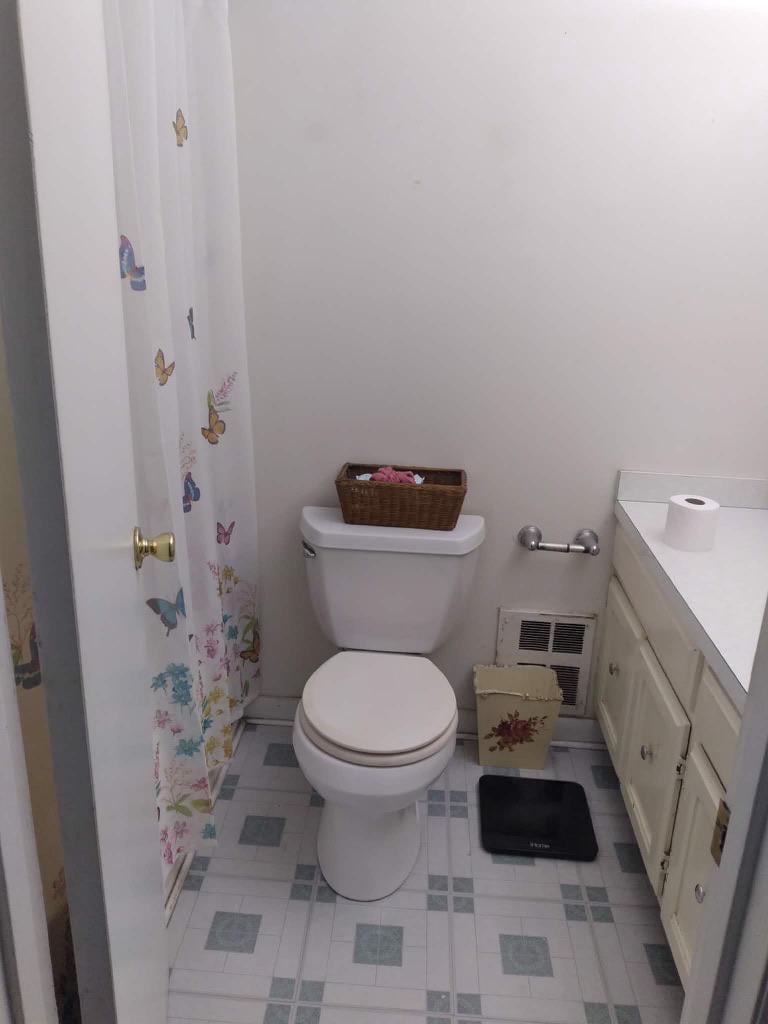 Bathroom with a white toilet, cream vanity, gray patterned tile floor, and floral shower curtain.