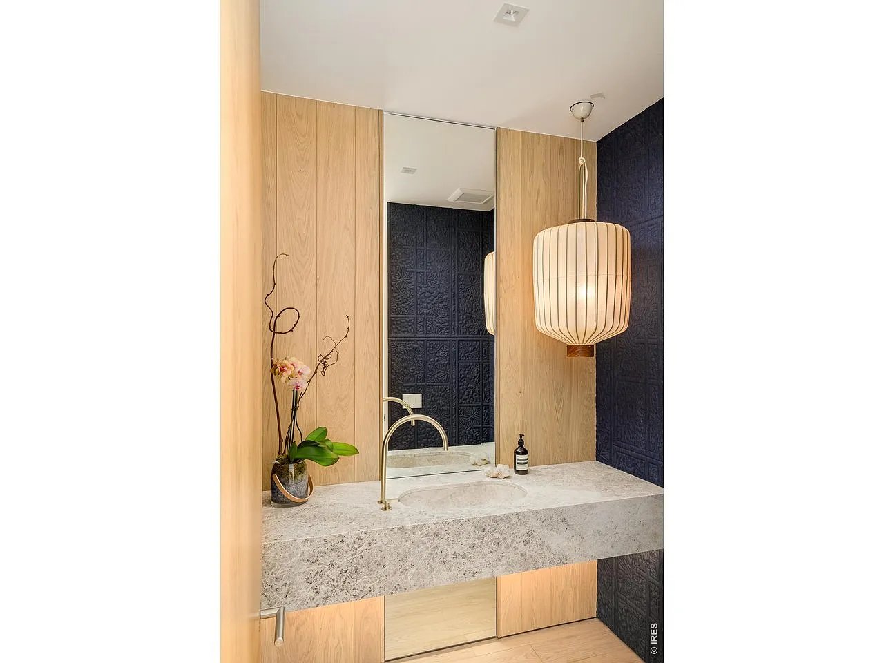 Bathroom vanity with an integrated stone sink, brass faucet, wood cabinetry, dark tile, and pendant light.