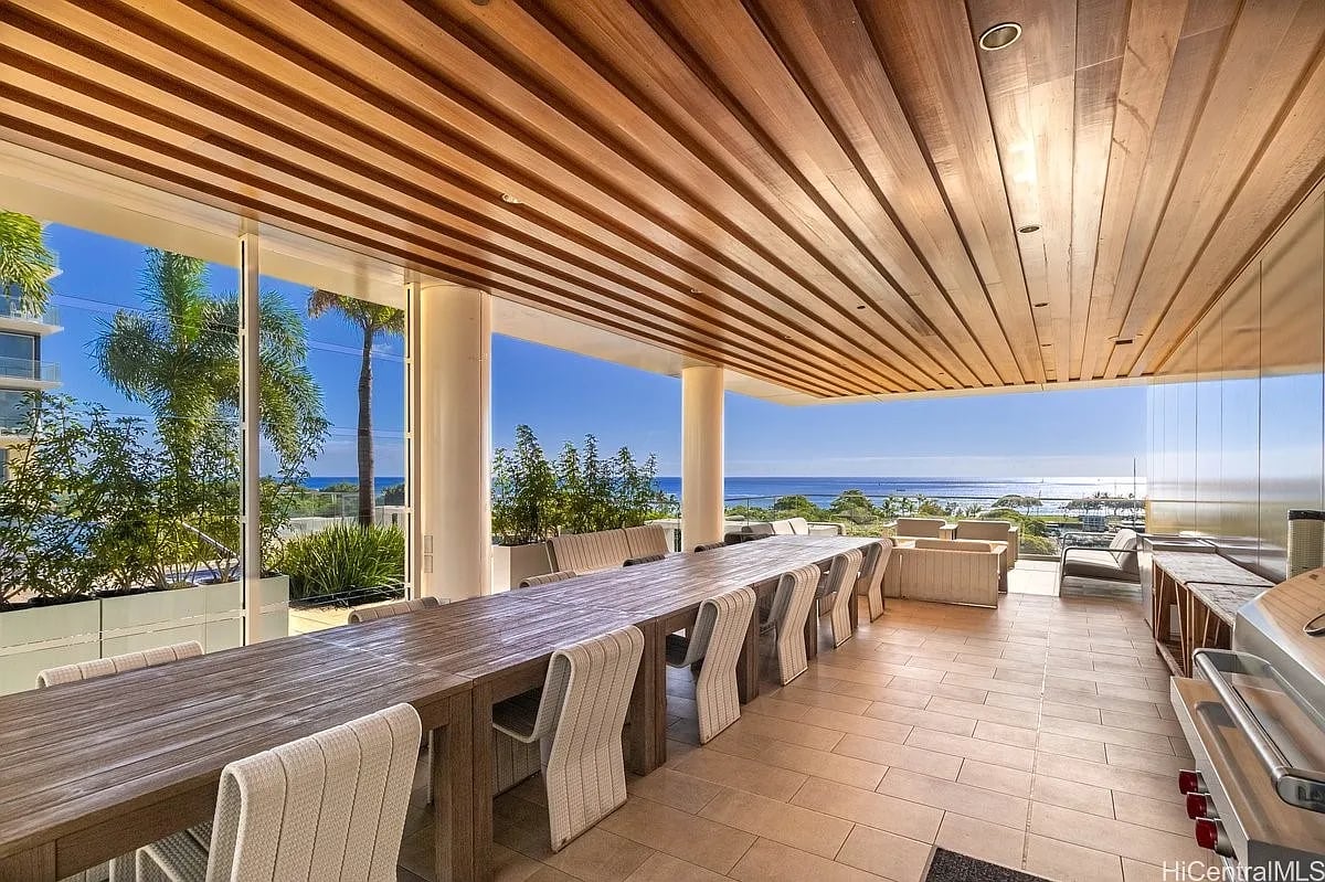 Covered ocean-view terrace with a long dining table, cushioned chairs, and built-in grill.