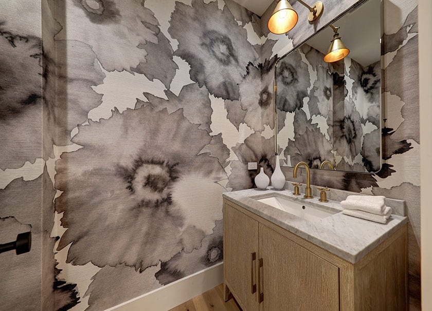 Bathroom vanity with bold gray floral wallpaper, marble countertop, and brass fixtures.