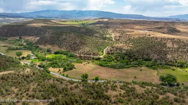 Aerial view of rolling hills near Silt, with green valleys, winding roads, and distant mountains.