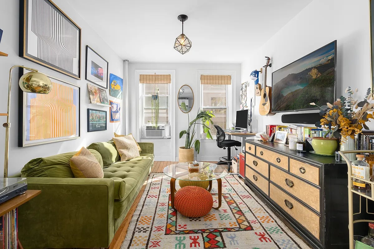 Furnished living room with a green tufted sofa, colorful patterned rug, and framed wall art.