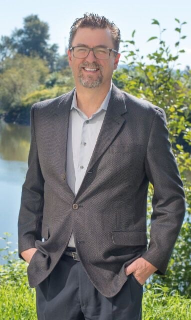 Marty Meyer in a dark blazer beside a pond with greenery behind him.
