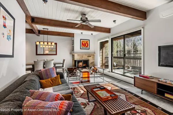 Living room with exposed wood beams, a stone fireplace, and large sliding glass doors.