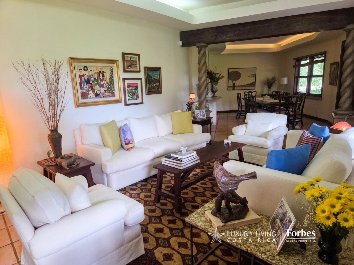 Living room with white sofas, colorful cushions, patterned rug, and an adjoining dining area.