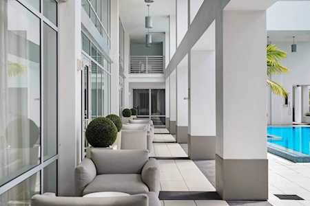 Modern covered patio with cushioned chairs and topiary beside a swimming pool.