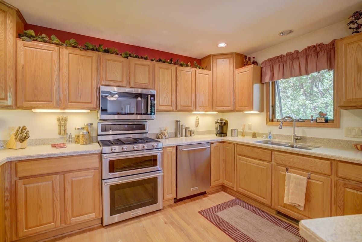 Kitchen with honey-colored wood cabinets, stainless steel double oven, and sink beneath a window.