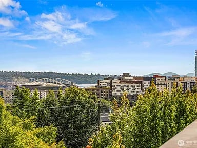 Seattle city view with leafy trees, mid-rise buildings, and a steel arch bridge.