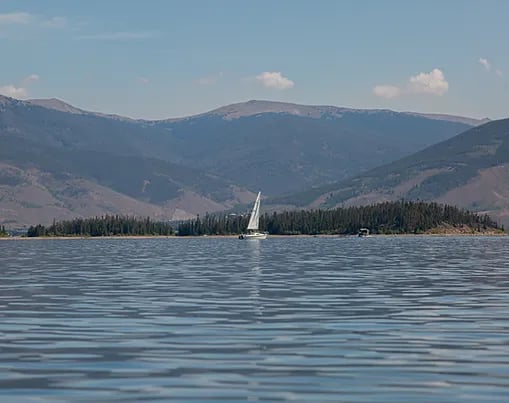 Sailboat on a mountain lake with forested shores and mountains in the distance.