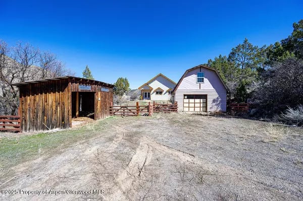 Rural home with an attached garage, fenced yard, and weathered wooden outbuilding.