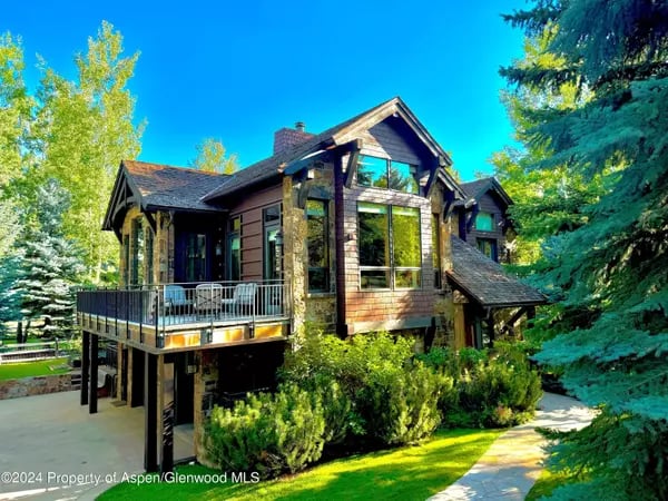 Mountain-style home with a raised deck, expansive windows, and mature trees.