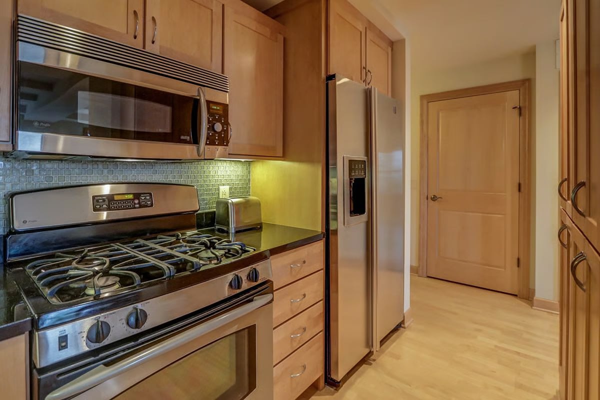 Kitchen with light wood cabinets, stainless appliances, a gas range, and a square-tile backsplash.