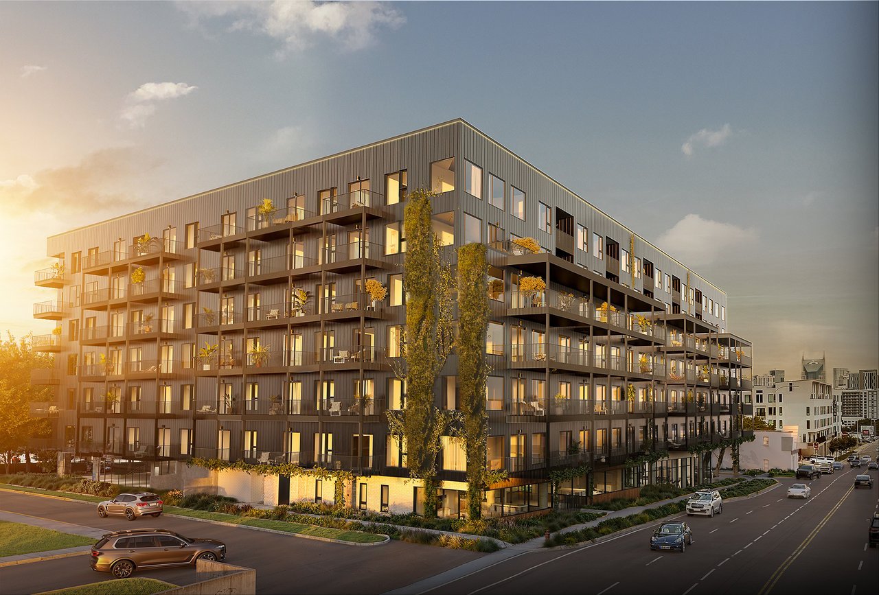Modern multi-story apartment building with glass balconies and landscaped street frontage at sunset.
