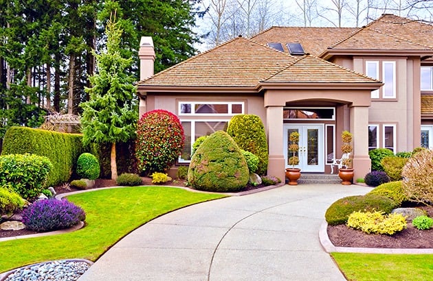 Tan two-story house with a curved driveway, manicured landscaping, and solar panels on the roof.