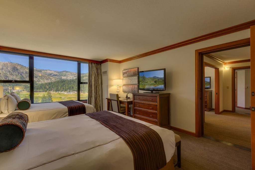 Resort condo bedroom with two beds and large windows overlooking a mountain valley.
