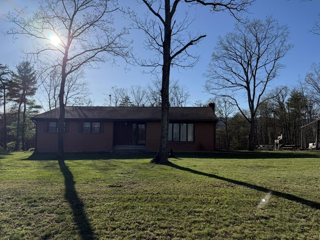 Single-story brick house beyond a broad lawn, framed by tall leafless trees.