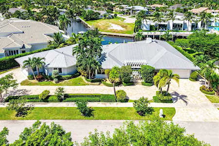 Aerial view of a single-story home with a light roof, palm trees, and a long driveway.